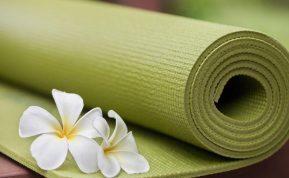 Žalias jogos kilimėlis suvyniotas su balta gėle