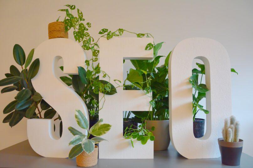 a white sign with plants and a potted plant next to it